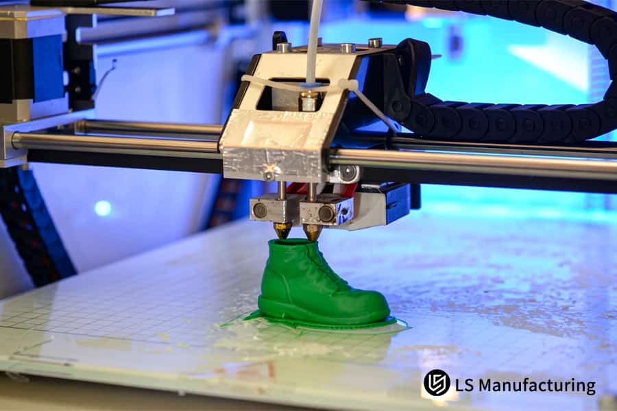 A 3D printer extrudes green TPR filament to build a small rubber boot prototype.