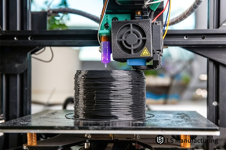 L'ugello di stampa 3D FDM estrude materiale filamentoso nero per formare un componente cilindrico solido.