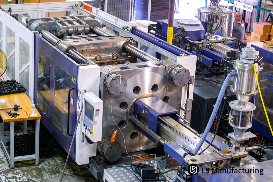A large tonnage injection molding press with a silver hopper processes polymer pellets for mass production.