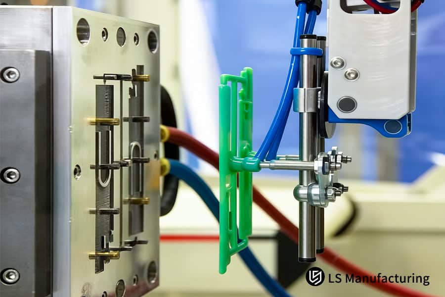 Un braccio robotico posiziona le parti in plastica verde nelle cavità metalliche per l'automazione del servizio di sovrastampaggio con inserti.