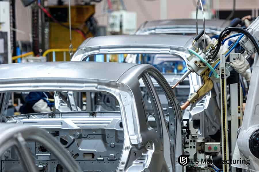 A robotic arm injects molten ABS resin into a silver door panel mold for automotive interior assembly.
