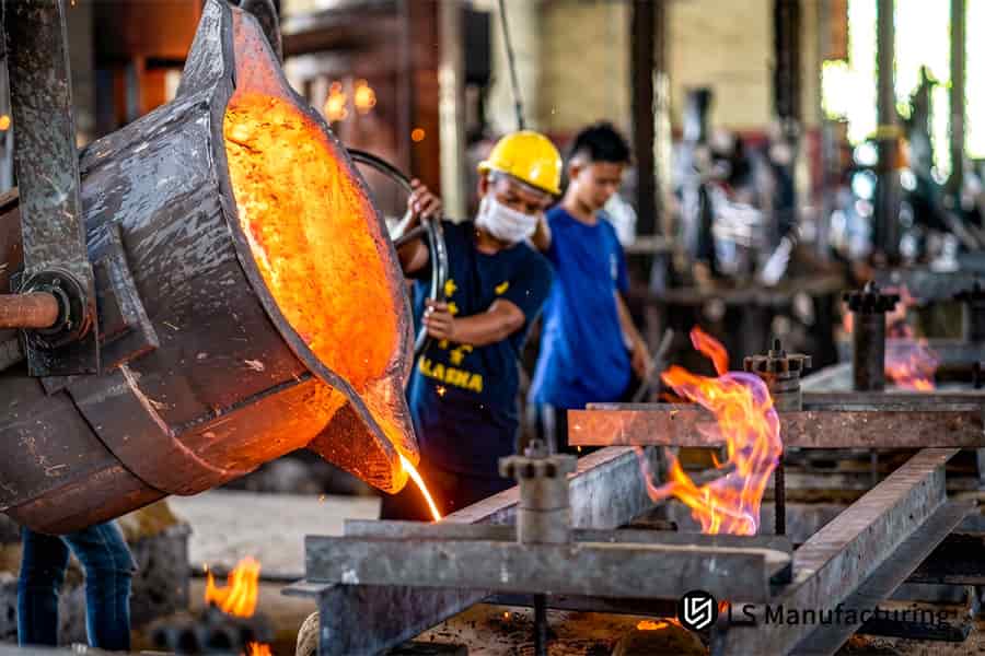 PPE を着用した鋳造作業員が、過熱したねずみ鉄を頑丈なコープ フラスコとドラッグ フラスコに注ぎます。